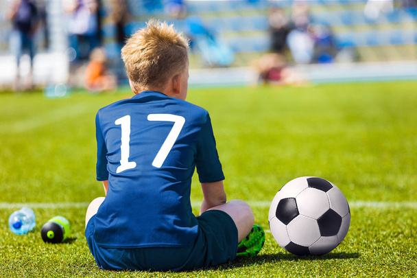 Fiatal foci focista. A kisfiú ül a focipálya. Ifjúsági labdarúgó kék Soccer Jersey - Fotó, kép