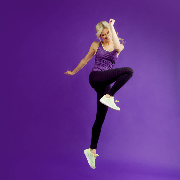 Beautiful young girl in a pose runner. Studio background, purple. Happy jumping - Foto, imagen