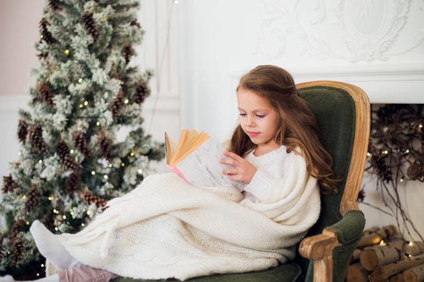 Little girl reading book near Christmas tree - Photo, Image