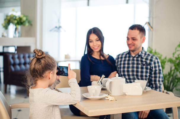 Rodina, rodičovství, technologický koncept lidí - zblízka šťastné matky, otce a holčička na večeři, kid pořizování Foto smartphone v restauraci - Fotografie, Obrázek
