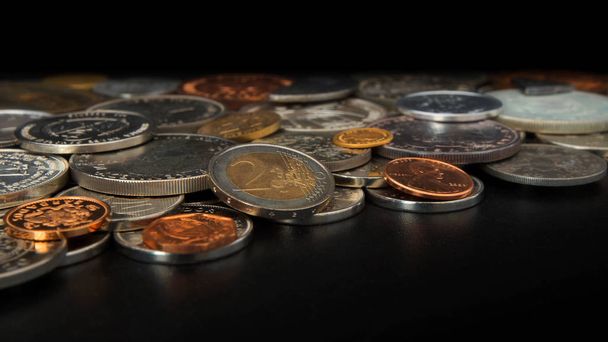 Vista lateral de una gran cantidad de monedas de diferentes países del mundo desordenado en la mesa negra. Enfoque en moneda de 2 euros - Escena numismática
 - Foto, Imagen