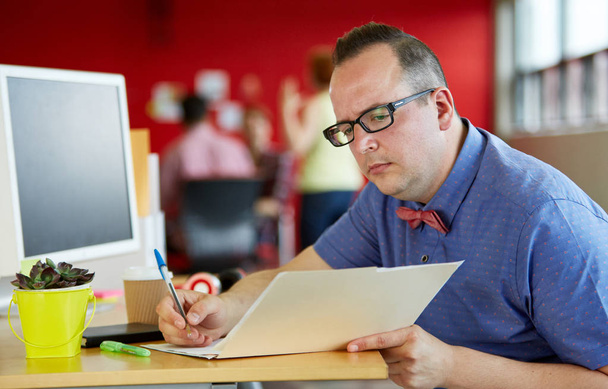 selbstbewusster männlicher Designer mit einem Ordner in roten kreativen Büroräumen - Foto, Bild