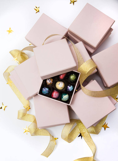 Chocolate hand painted luxury candy bonbons in a pink gift boxes and golden ribbon. White background with golden stars.  - Valokuva, kuva