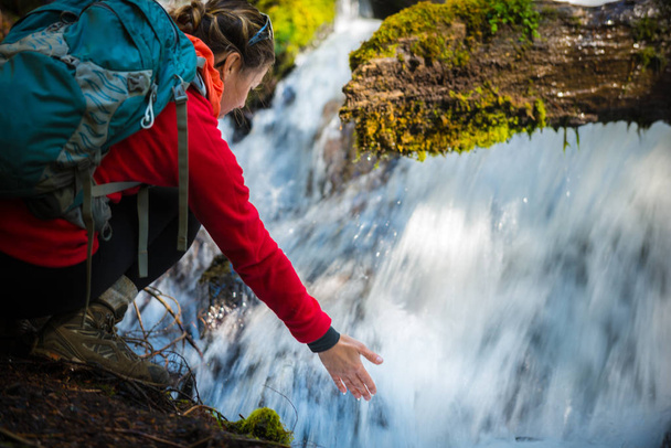 Backpacker holding hand under running water of clearwater falls  - 写真・画像