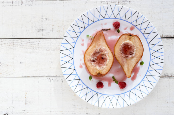 Sweet Baked pear stuffed with cottage cheese with raspberry syrup and fresh raspberries in sugar. Dessert on a white wooden background. The top view. - Photo, image