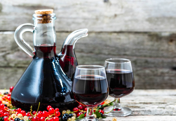 Glass wine bottle on wooden table. Sweet alcohol made from fruits many variety berries currant - Photo, Image