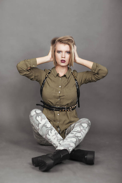 Portrait of 20s years old woman in military style clothes sitting and titivating hair  - Foto, Imagem
