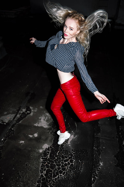 Outdoor portrait of young beautiful happy blond european lady posing on street at night. Model wearing stylish clothes red pants and jump. Female fashion. City night lifestyle. Copy space. - Foto, afbeelding