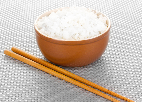 Bowl of rice and chopsticks on grey mat - Foto, afbeelding