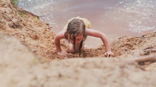 Lachende schattig klein meisje in een duik pak kruipen op een strand en springen in het water. Ze heeft plezier. - Video