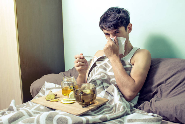 молодой человек лежит в постели больной простудой и гриппом
 - Фото, изображение