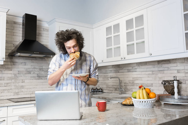 Hombre comiendo desayuno durante el uso de ordenador portátil
 - Foto, Imagen