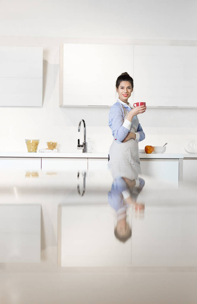 Woman drinking coffee in her kitchen - Фото, изображение