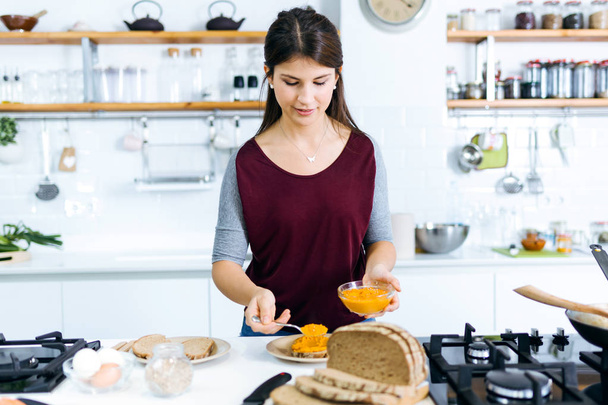 Beautiful young woman preparing toast with mashed vegetables in the kitchen. - Foto, imagen