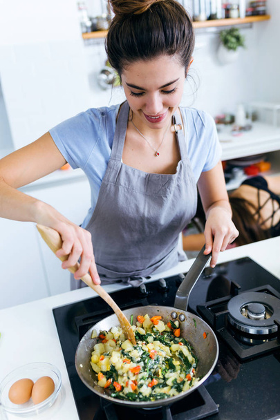 Young woman mixing chards, potatoes, red pepper and eggs into the pan. - Foto, imagen