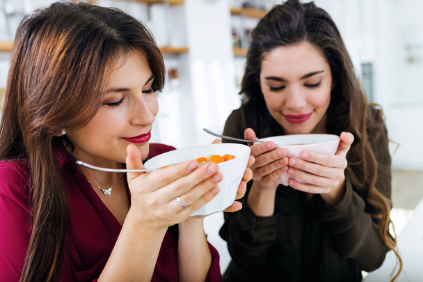 Dos hermosas mujeres jóvenes comiendo sopa de verduras en la cocina
. - Foto, Imagen