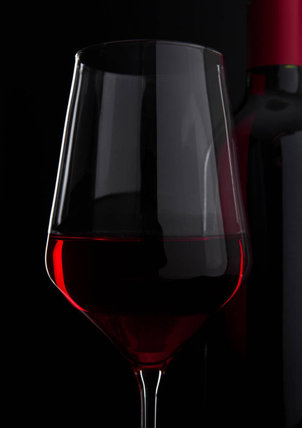 Copa de vino tinto con botella de cerca en negro
 - Foto, imagen