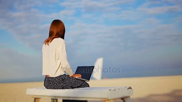 Tyttö työskentelee kannettavan aurinkoisella rannalla
 - Materiaali, video