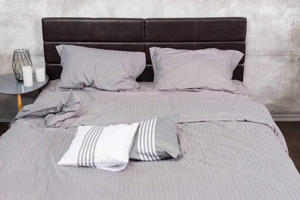 Stylish bed with grey colors and bedside table with many candles - Фото, изображение