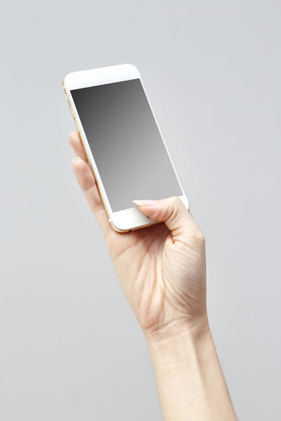 Gros plan d'une femme tapant sur un téléphone portable isolé sur fond blanc, main de fille tenant un smartphone moderne et pointant avec figer, écran blanc pour le mettre sur votre propre page Web ou message
. - Photo, image