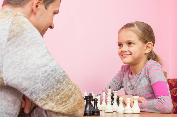 Pai e filha alegremente olham um para o outro, jogando xadrez
 - Foto, Imagem