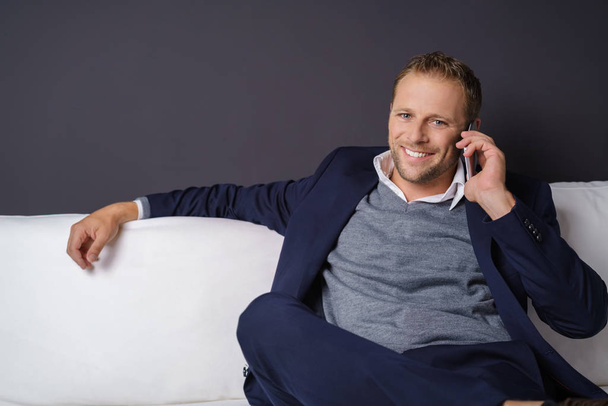 Confident man sitting on a sofa taking a call on his mobile - Foto, Bild