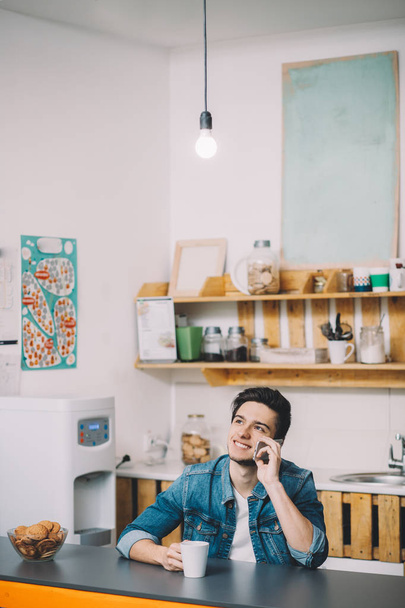 Young Man Relaxing Sitting In Kitchen Talking On Phone - 写真・画像