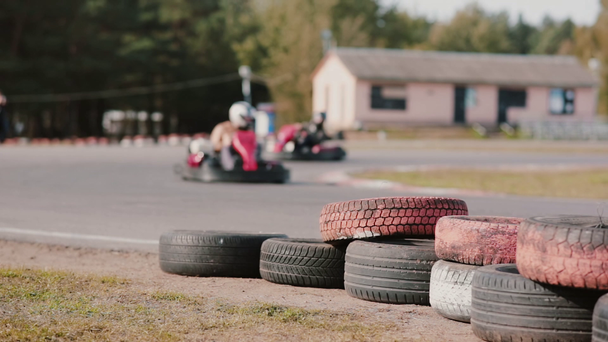Kartfahrer bewegen sich auf einer Kartbahn. Farbige Reifen in der Nähe der Strecke. - Filmmaterial, Video