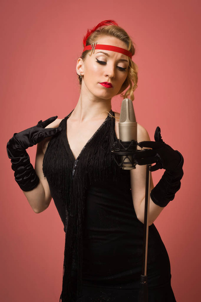 Pretty actress in black retro dress singing with microphone - Foto, afbeelding