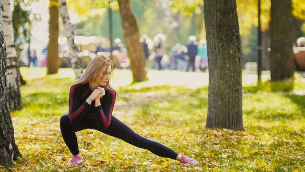 Sexy aantrekkelijke vrouwelijke blonde bikini-fitness model die zich uitstrekt in het najaar park op grond vallen gele bladeren - flexibiliteit van de benen - Foto, afbeelding