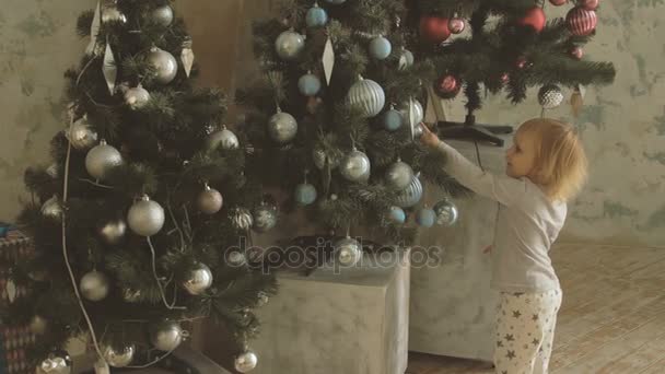 Kis aranyos lány pont a ujj karácsonyi golyókat díszített fa - Felvétel, videó