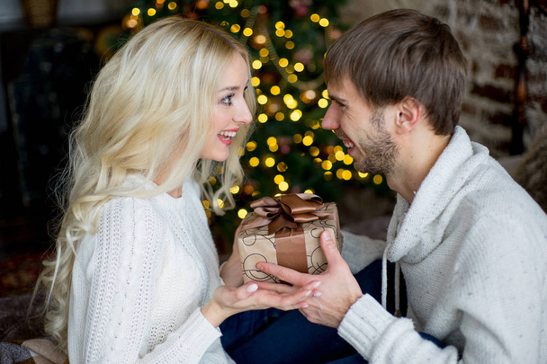 Happy couple of lovers in white pullovers give each other gifts - 写真・画像