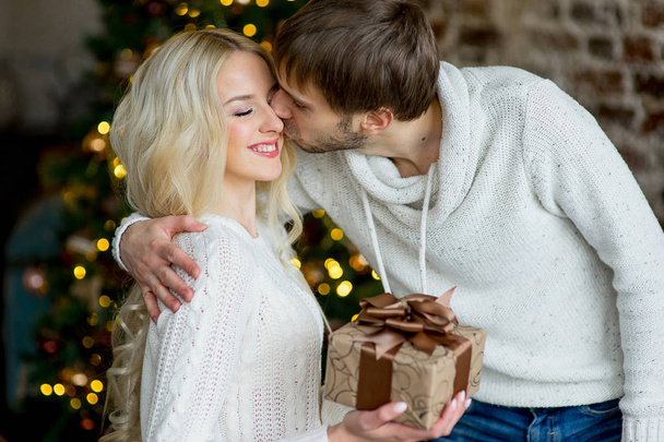 Happy couple of lovers in white pullovers give each other gifts - Photo, Image