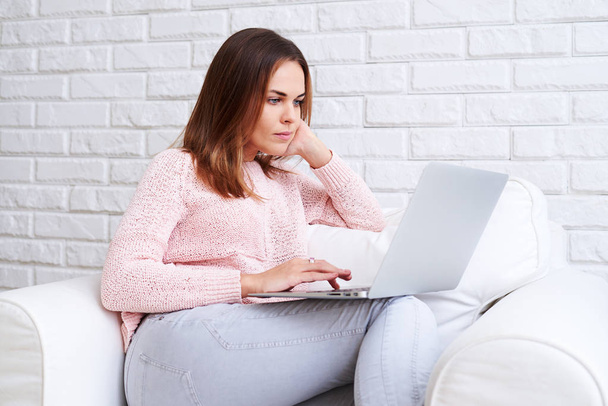 Poważny kobieta siedzi wygodnie i trzymając laptop  - Zdjęcie, obraz