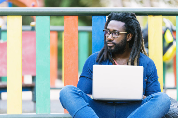 Portrait of african man sitting outside with laptop. - Fotó, kép