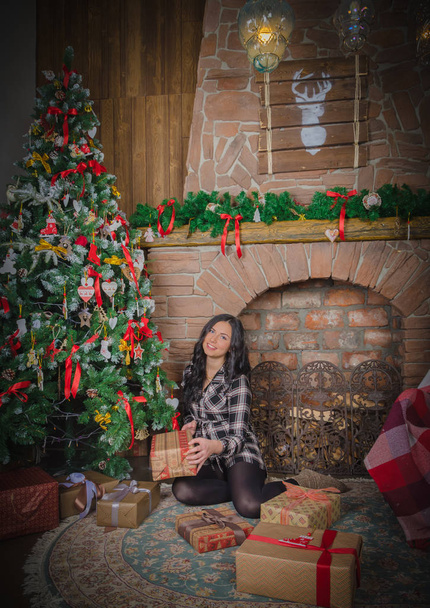Christmas beautiful girl sitting near the fireplace and rejoice in the gifts. - Foto, imagen