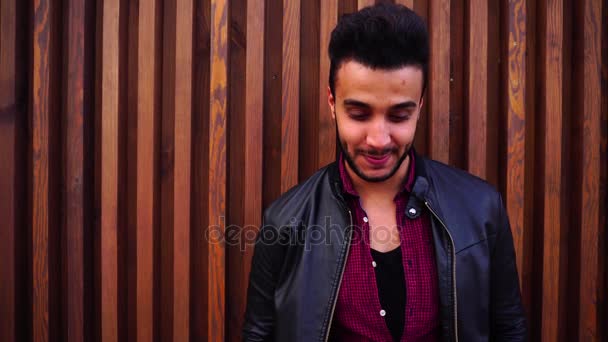 Mooie Arabische jongeman Stands in de buurt van de muur en glimlacht, lacht, ziet er op de Camera en aan de zijkant op achtergrond van trappen in openlucht. - Video