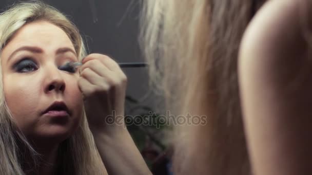 Beautiful blonde girl making evening make-up near the mirror - Materiał filmowy, wideo