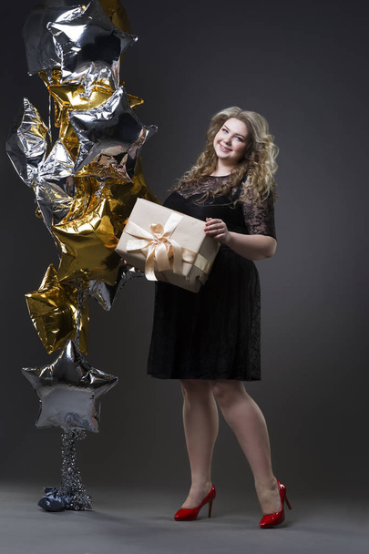 Young beautiful plus size model in black dres with gift box, xxl woman on gray studio background - Photo, Image