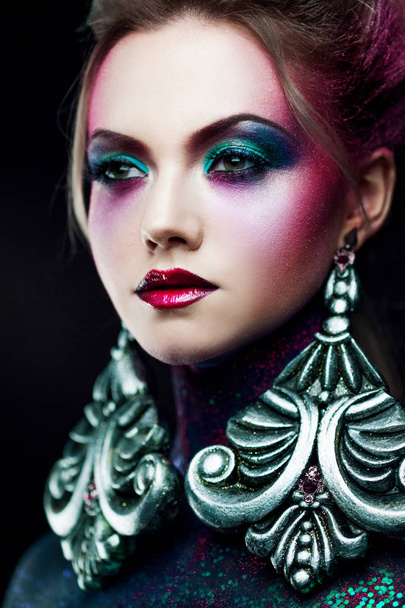 Young attractive blonde girl in bright art-makeup, high hair, body painting. Rhinestones and glitter - Фото, изображение