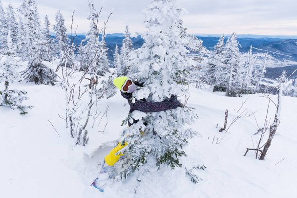 Young woman in bright yellow cap, ski mask and on snowboard embr - Foto, afbeelding