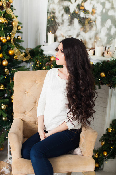 Young beautiful pregnant woman siting in a Christmas setting. - Foto, imagen