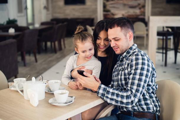 családi, szülői, technológia emberek koncepció - boldog anyja, apja és kislány figyelembe selfie smartphone étteremben vacsorázik - Fotó, kép