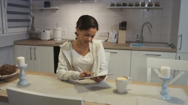 A beautiful young African American woman using a tablet computer in a kitchen. - Кадры, видео