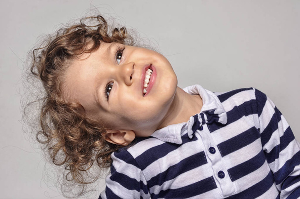 Beautiful curly toddler looking up and smiling happy with his white teeth - Valokuva, kuva