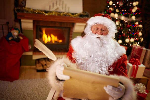 Santa Claus sitting and reading children wishes for Christmas - Foto, Imagem
