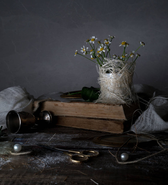 vintage books lying on a rustic wooden shelf with  bouquet of daisies. Country still life. - 写真・画像