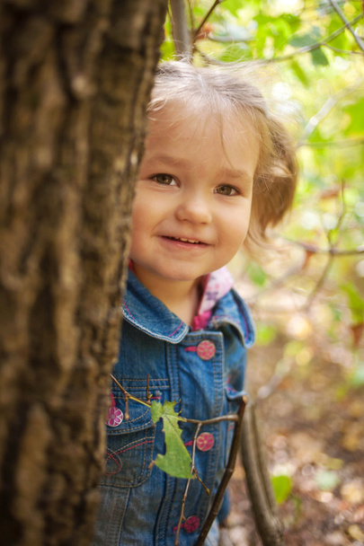 kleines Mädchen lächelt und schaut vom Baum - Foto, Bild