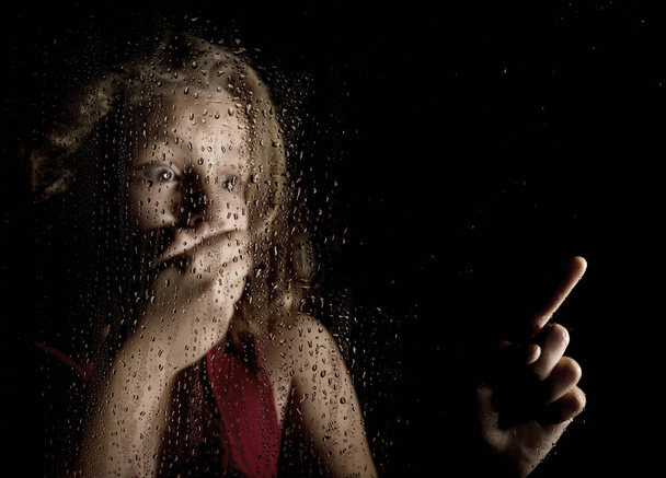 μοναχική κοπέλα θλιβερό πίσω από το παράθυρο με σταγόνες. φοβισμένη νεαρή γυναίκα δείχνει κάτι - Φωτογραφία, εικόνα