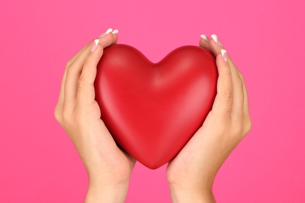 Corazón rojo en las manos de la mujer, sobre fondo rosa de cerca
 - Foto, Imagen